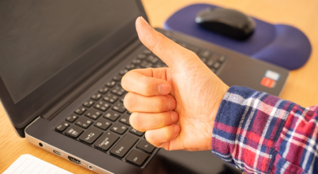 パソコンの上でグッドのハンドサインをしている男性